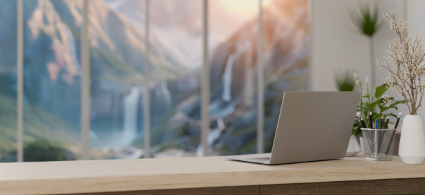 在一间现代化的办公室里，桌子上放着一台笔记本电脑，窗户大得惊人，可以看到雪山的景色。图片下载