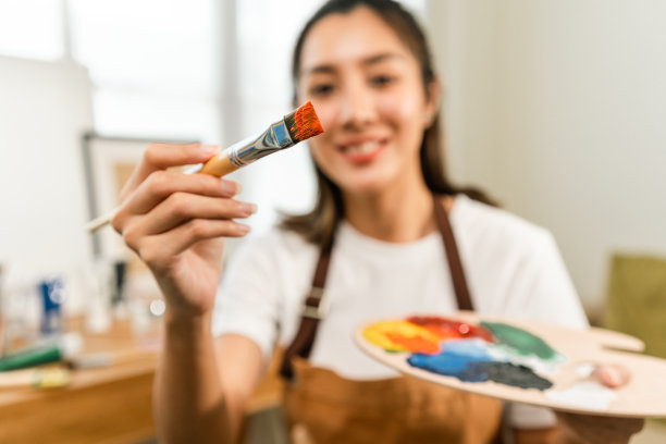 亚洲女艺术家正在用画笔和不同的丙烯酸颜料作画。作为艺术概念的女艺术家在创作工作室的画布上作画图片下载