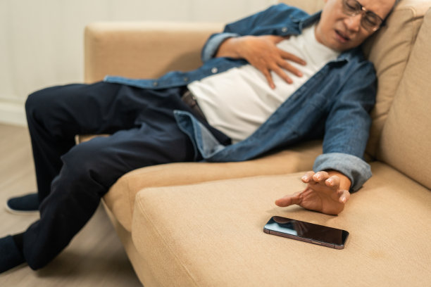 年长的老人感到胸口一阵疼痛，他握了握他的手，捏了捏。需要治疗的心脏病发作倒在沙发上。需要帮助请用手机拨打紧急救援电话图片下载