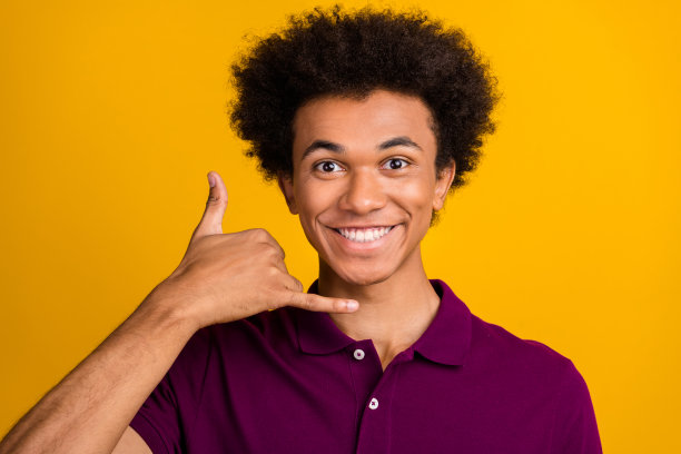 照片中开朗微笑的男子穿着洋红时尚的衣服，手臂显示手机打电话给我的手势孤立在黄色背景图片下载