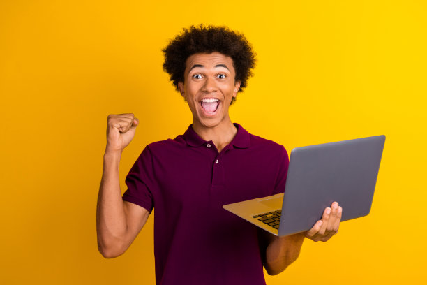 照片中的快乐男子穿着时髦的马球，举手庆祝盈利购买现代上网本孤立在黄色的背景图片下载