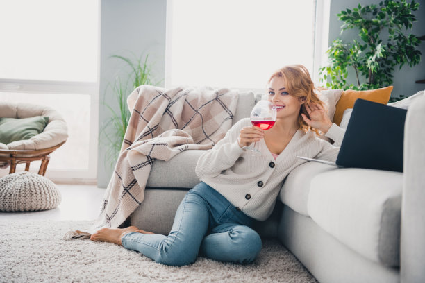 令人惊叹的宁静女士全身照片坐地毯地板喝酒用笔记本电脑幻想自由时间明亮的室内公寓图片下载