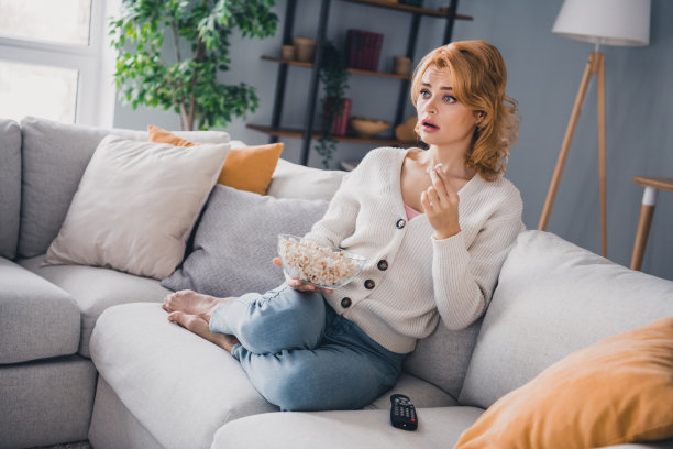 无言以对的女士全身照片赤脚坐在沙发上拿着爆米花碗看电影电视公寓里面图片下载