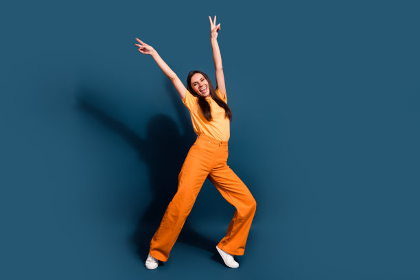 深色皮肤的西班牙裔女士的全身照片举起双手，做了两个v手势，宣传深蓝色背景上的衣服图片下载