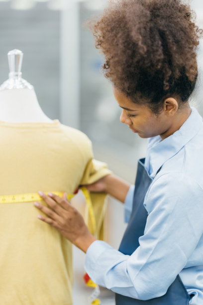 一位美国女裁缝用卷尺设计人体模型，准备在机器上缝制衣服，然后用一卷线把衣服缝制出来。图片下载