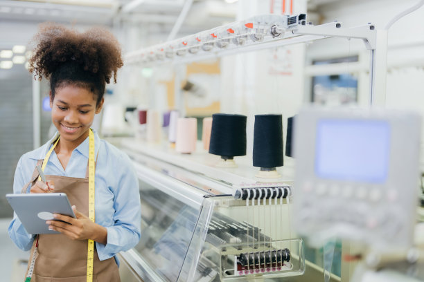 一位美国女裁缝设计师用一支笔写下服装项目，并有一台电脑织布机和线工作。寄给时装秀的组织者图片下载