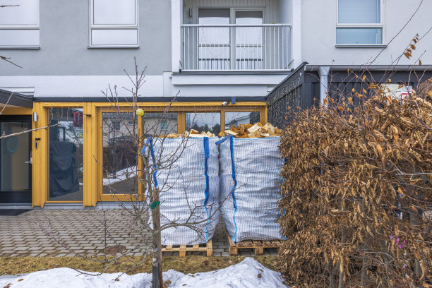 一个冬春时节，别墅前的花园里，用桦木柴火堆在托盘上的运输袋。瑞典。图片下载