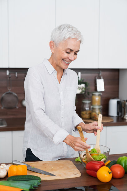 竖版照片：在家中厨房烹饪蔬菜沙拉的中年妇女图片下载