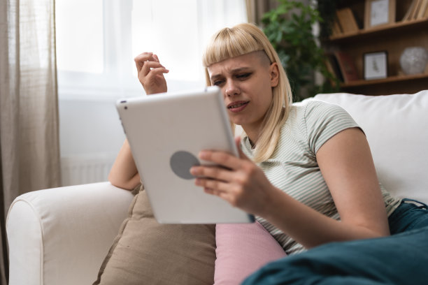 快乐的千禧一代金发少女在家里拿着平板电脑查看社交媒体微笑的年轻女子使用设备应用玩游戏网上购物订购送货在沙发上放松。网上约会图片下载
