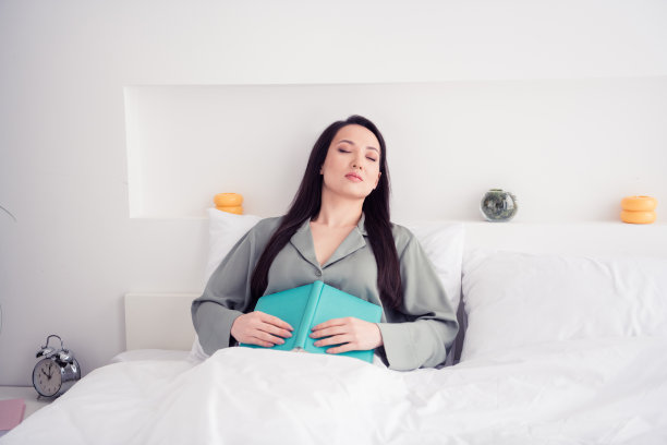照片肖像迷人的年轻女子躺着看书睡觉穿着时髦的灰色睡衣隔离在白色现代室内设计图片下载