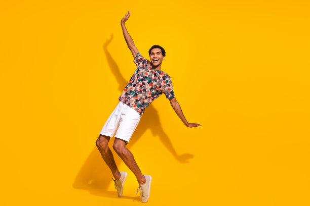 年轻英俊的旅游男友的全身照片，在黄色的背景下，踮着脚尖摔倒，试图保持平衡图片下载