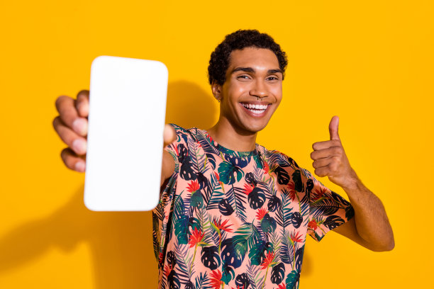 年轻英俊的男子享受省钱旅行更便宜的照片显示大拇指在智能手机上孤立的黄色背景符号图片下载