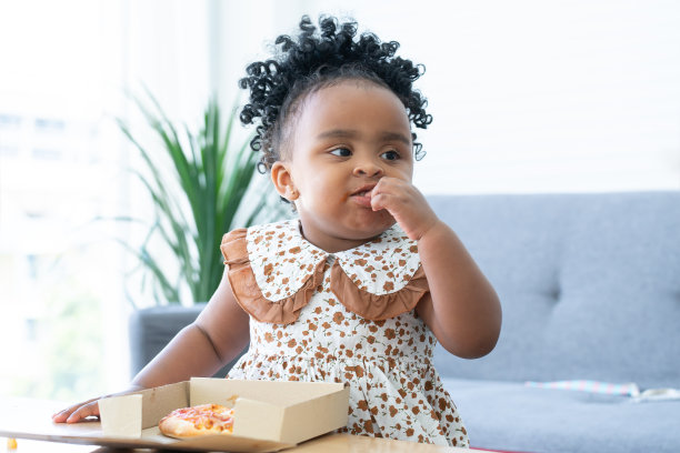 可爱的非洲孩子在家吃披萨的照片。孩子们享受和享受美味的午餐。快乐的小女孩有一张漂亮的脸，用手拿着披萨吃图片下载