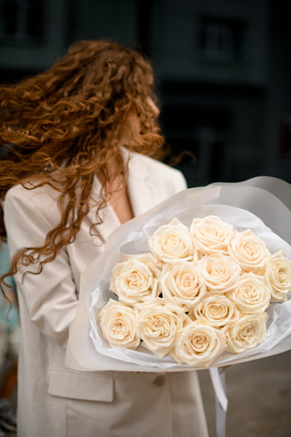 侧视图时髦的女孩与红色卷曲的头发在白色夹克与一束玫瑰图片下载
