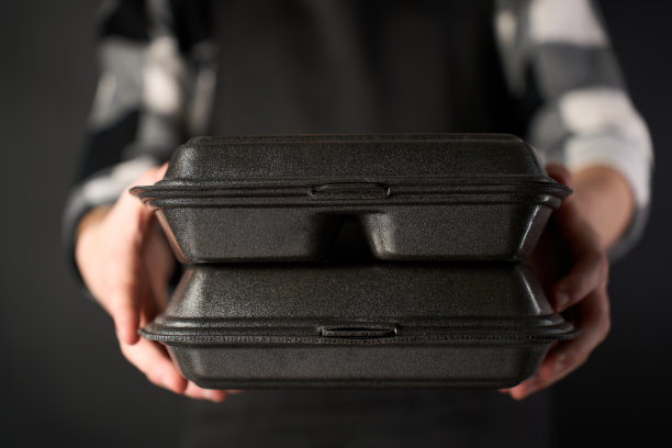 男厨师拿着午餐盒，手里拿着食物，黑色背景。图片下载