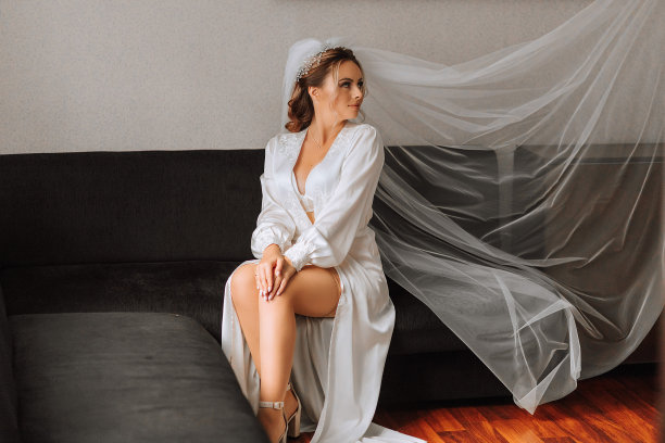 新娘身着白色缎子礼服，专业的发型和妆容，戴着长长的面纱。婚礼的前一天早上。图片下载