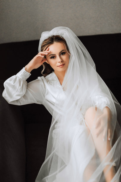新娘身着白色缎子礼服，专业的发型和妆容，戴着长长的面纱。婚礼的前一天早上。图片下载