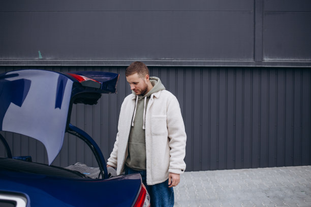 年轻的商人在乡下看汽车后备箱的全长侧视图。图片下载