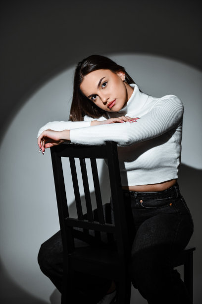 穿着白色高领毛衣坐在椅子上目光锐利的女性图片下载