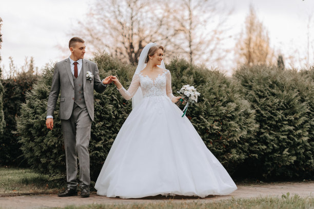 新郎和新娘手牵着手在高高的绿树中散步。广角秋日照片。宽松的婚纱。新郎的经典西装图片下载