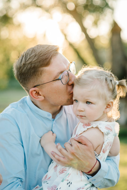 爸爸亲吻孩子，花时间在一起。夕阳下，爸爸在公园拥抱小女孩。一个初学走路的女儿在暑假的田野里拥抱父亲的照片。友好家庭的概念。特写镜头图片下载