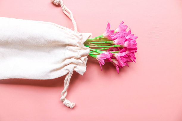 俯视图照片的花束粉红色的百合在一个串袋孤立的粉红色背景与copyspace。春花在粉红色的平地上躺着。贺卡，节日概念。西风花图片下载