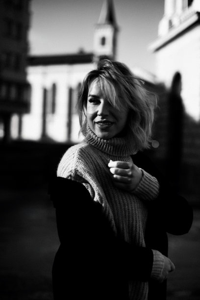 黑白照片中，穿着毛衣的自信女人站在大楼旁。时尚的女性肖像与双手放在臀部。都市生活理念与都市时尚女性。图片下载