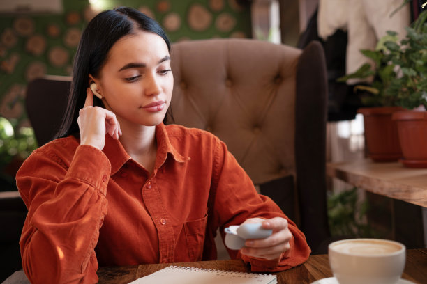 在咖啡馆放松时，戴着耳机的女孩坐在那里，拿着无线耳机的充电盒图片下载