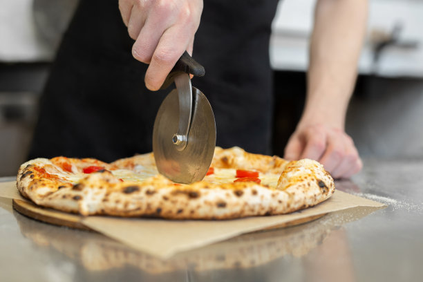 餐厅厨房里，厨师-面包师手切披萨的特写。图片下载
