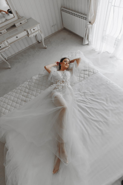 一个漂亮的女孩，梳着婚礼的发型，头上戴着头饰，穿着透明的长袍，躺在皇家室内酒店的床上。长面纱，自然光，人像照片图片下载