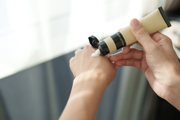 在这张剪短的图片中，一位中年亚洲女性正在用润肤霜涂抹双手干燥的皮肤，阳光温柔地照在她的皮肤上，突显出滋养的姿态。图片下载