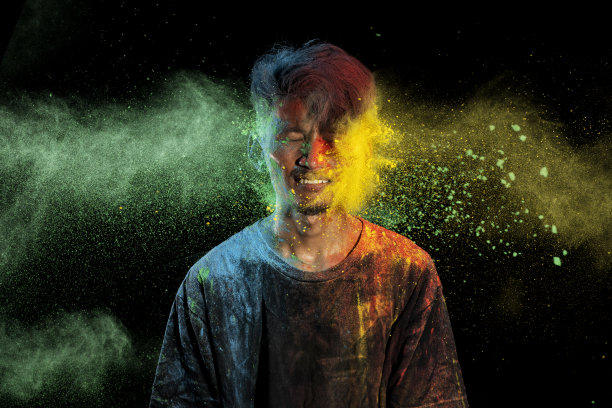 一名亚洲男子身上洒满了五彩缤纷的胡里节粉末，在黑色的背景上玩得很开心。图片下载