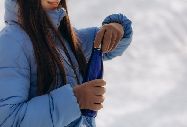 年轻漂亮的女孩戴着帽子和连指手套，在冬天喝着热水瓶里的热茶。图片下载