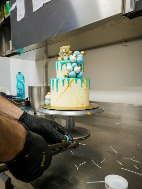 年轻的糕点师正在为一个婴儿的生日装饰一个双层的霜白色绿松石滴蛋糕图片下载