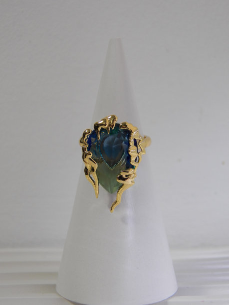 白色背景上戒指的特写照片。一枚镶着黄蓝色宝石的金戒指融化了图片下载