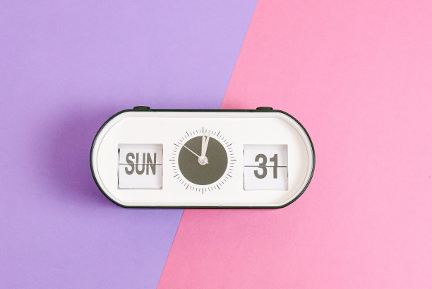 闹钟与时间和日期的复活节在紫丁香粉红色的背景。图片下载