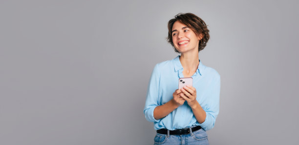 横幅照片，快乐的女商人在工作室里穿着智能休闲，同时使用智能手机和工作。年轻女性使用手机应用程序，阅读新闻，快速连接，搜索，下注，上网图片下载