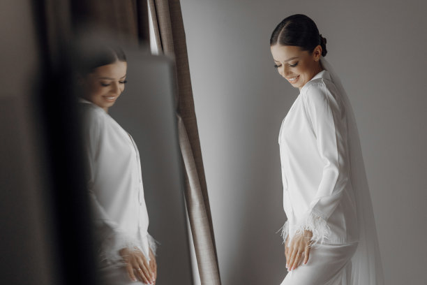 清晨穿着白色睡衣的年轻美丽的新娘。新娘在酒店的早晨。长长的时尚面纱。镜子照片图片下载