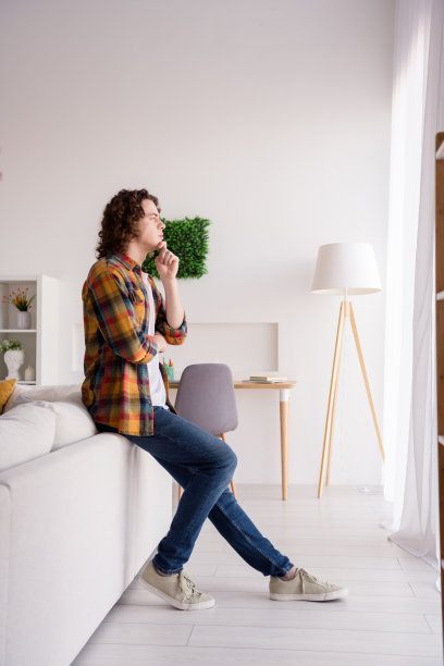 梦幻体贴的家伙穿格子衬衫的全长垂直照片手臂下巴看着窗户在室内房间家里的房子图片下载