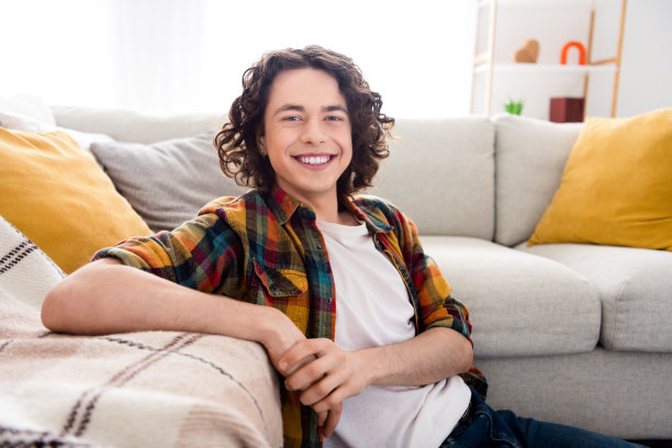 好心情的照片有趣的家伙穿着格子衬衫坐在地板上笑着洁白的牙齿在家里的房间里图片下载