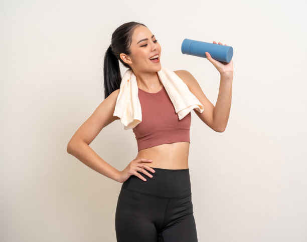 年轻美丽的亚洲女人穿着运动服，拿着一瓶水，孤立的背景。肖像快乐健康苗条的身材和坚定的拉丁迷人的运动妇女运动后喝水锻炼图片下载
