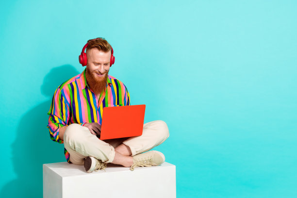 全身长度尺寸的照片，红色的头发有胡子的人专业在耳机编码使用上网本孤立的蓝色背景。图片下载