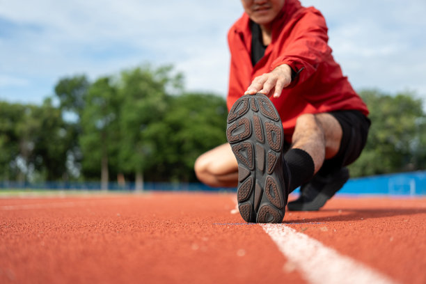 年轻的亚洲男子穿着运动服在户外跑步。印度男子在体育场跑道上跑步前伸展腿的照片。训练运动员在户外运动的概念。图片下载