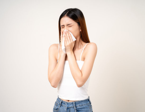 患有流鼻涕和高烧。寒热概念。美丽的年轻亚洲患病妇女的肖像在孤立的白色背景被围巾包裹打喷嚏。图片下载