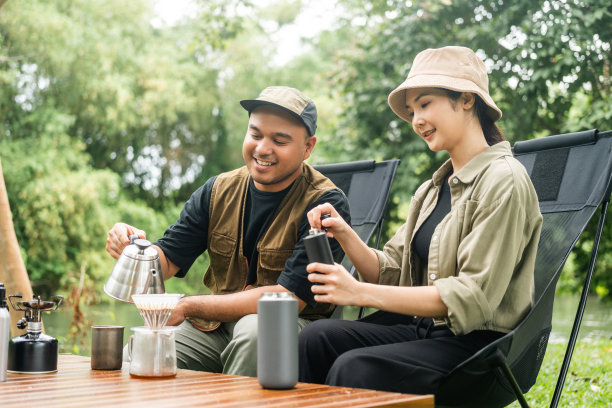 年轻的亚洲夫妇，男人和女人坐在户外露营地喝咖啡。两个人带着咖啡机工具在森林里露营。旅游，放松，露营，度假，假日，周末的主题图片下载