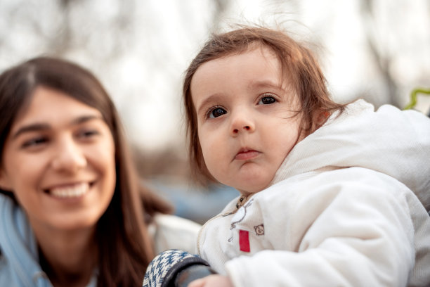 一张母亲和一岁女儿散步的照片。春天，可爱的女婴坐在户外的婴儿车里。带着小孩的家庭休闲。图片下载