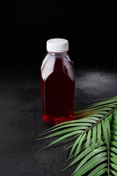 浆果饮料在黑色背景与叶子取出瓶。模拟饮料在最小的概念与黑色背景和棕榈叶。瓶装冷饮，用于展示包装。浆果酒。图片下载