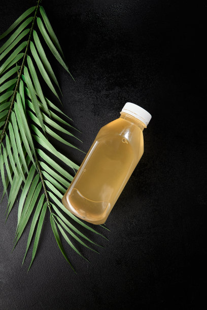 柠檬饮料在黑色背景与叶子取出瓶。模拟饮料在最小的热带概念与黑色背景和棕榈叶。瓶装冷饮，用于展示包装。图片下载