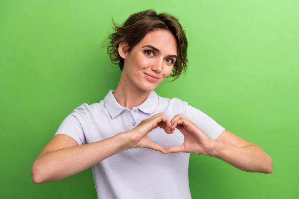 照片中可爱迷人的女士穿着polo t恤，胸前的手指上有爱心的象征，在绿色的背景上被隔离开来图片下载
