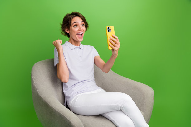 照片的快乐幸运的女士穿着灰色t恤赢得游戏现代小工具上升的拳头孤立的绿色背景图片下载